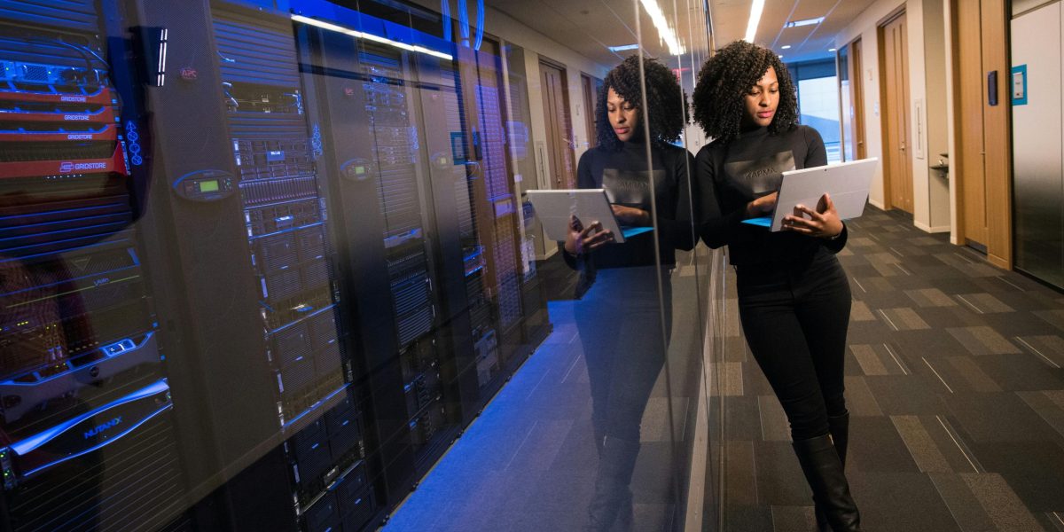 A woman using a laptop navigating a contemporary data center with mirrored servers.